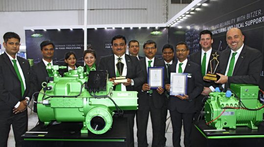 BITZER representatives stand together with the two ACREX prices behind BITZER compressors